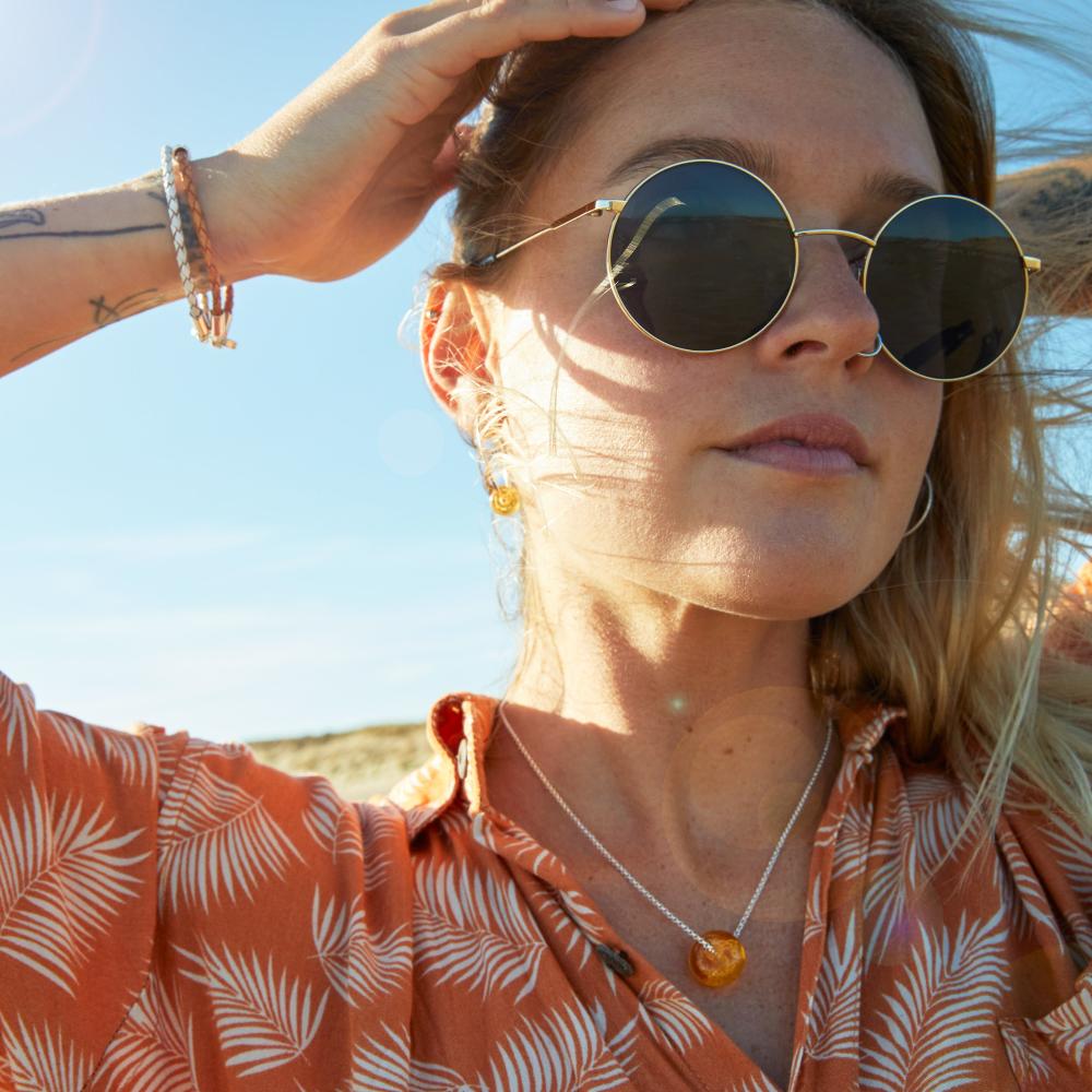 Girl in orange leaf patterned shirt, gold sunglass and glass bead necklace and bracelets, string on the beach.