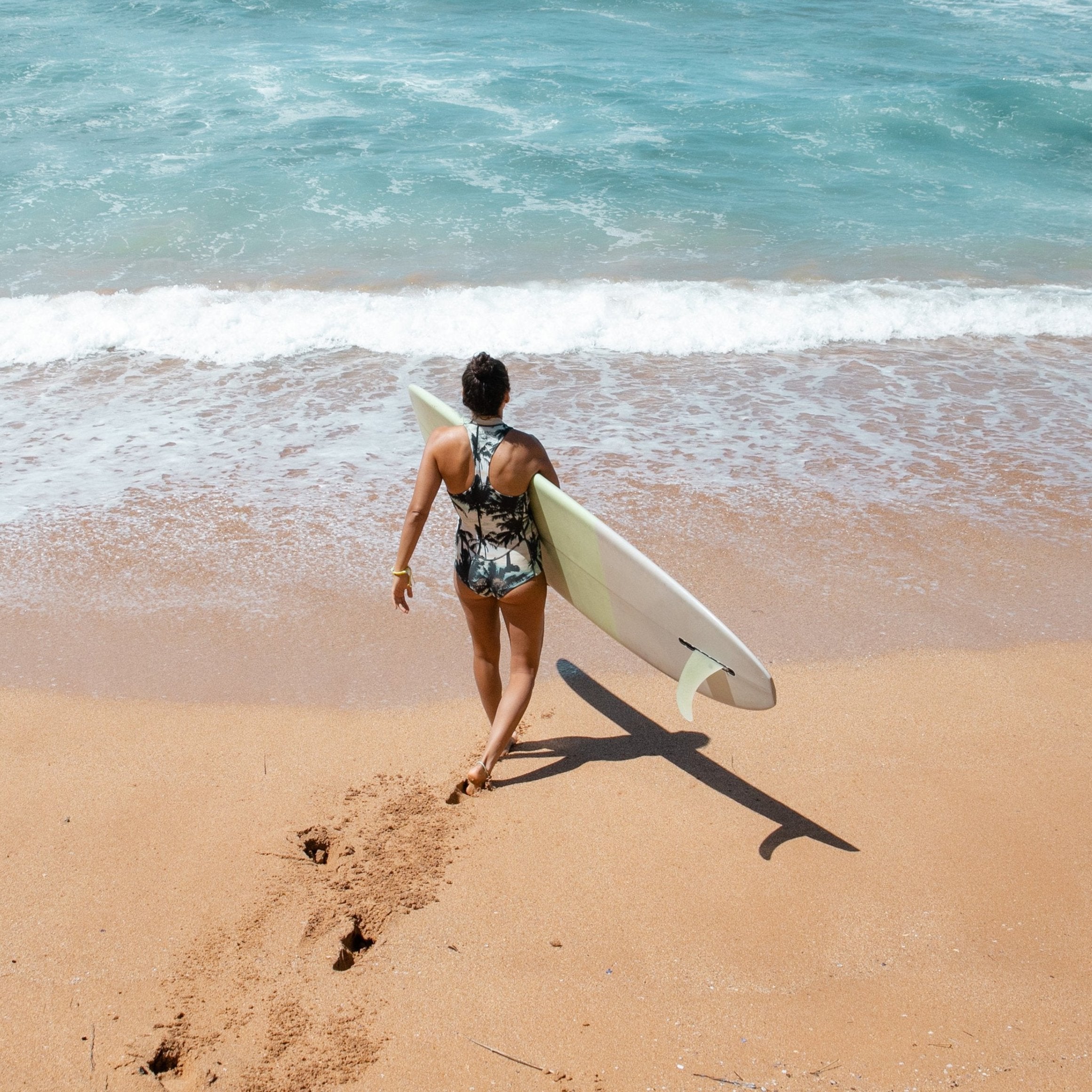 Surfer waling down sandy beach into water wearing Nalu beads bracelet.