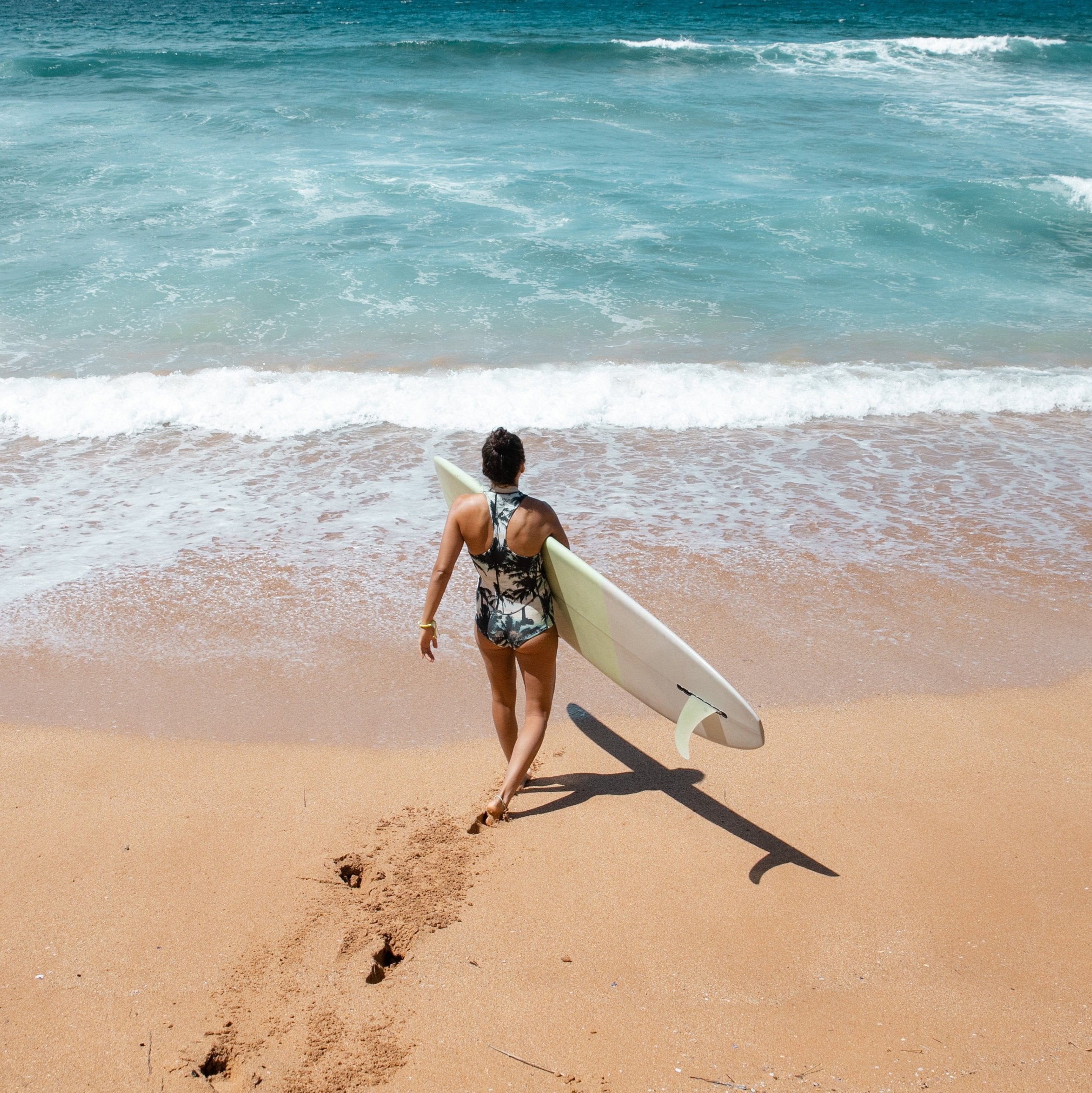 Women surfer walking into sea wearing beach inspired yellow bead bracelet.