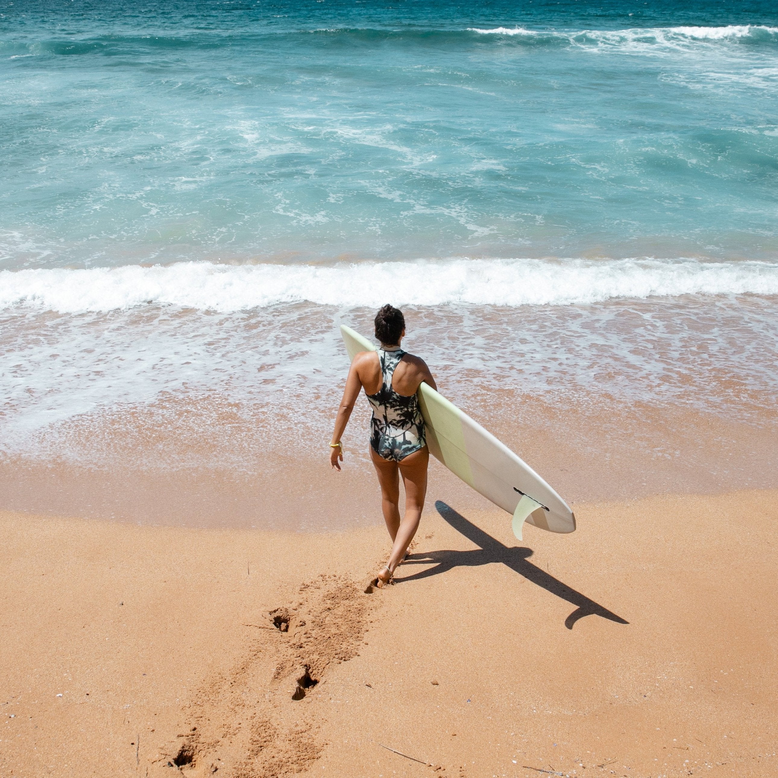 Surfer walking into the sea carrying surfboard.