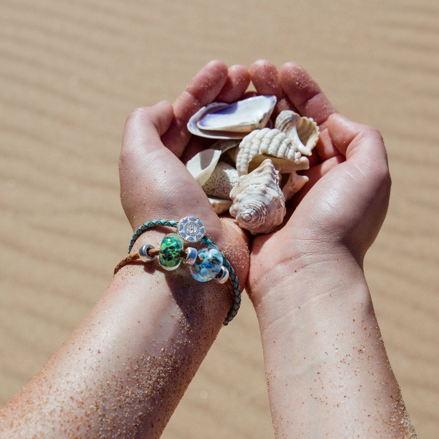 Hands holding shells wearing plaited leather bracelets.