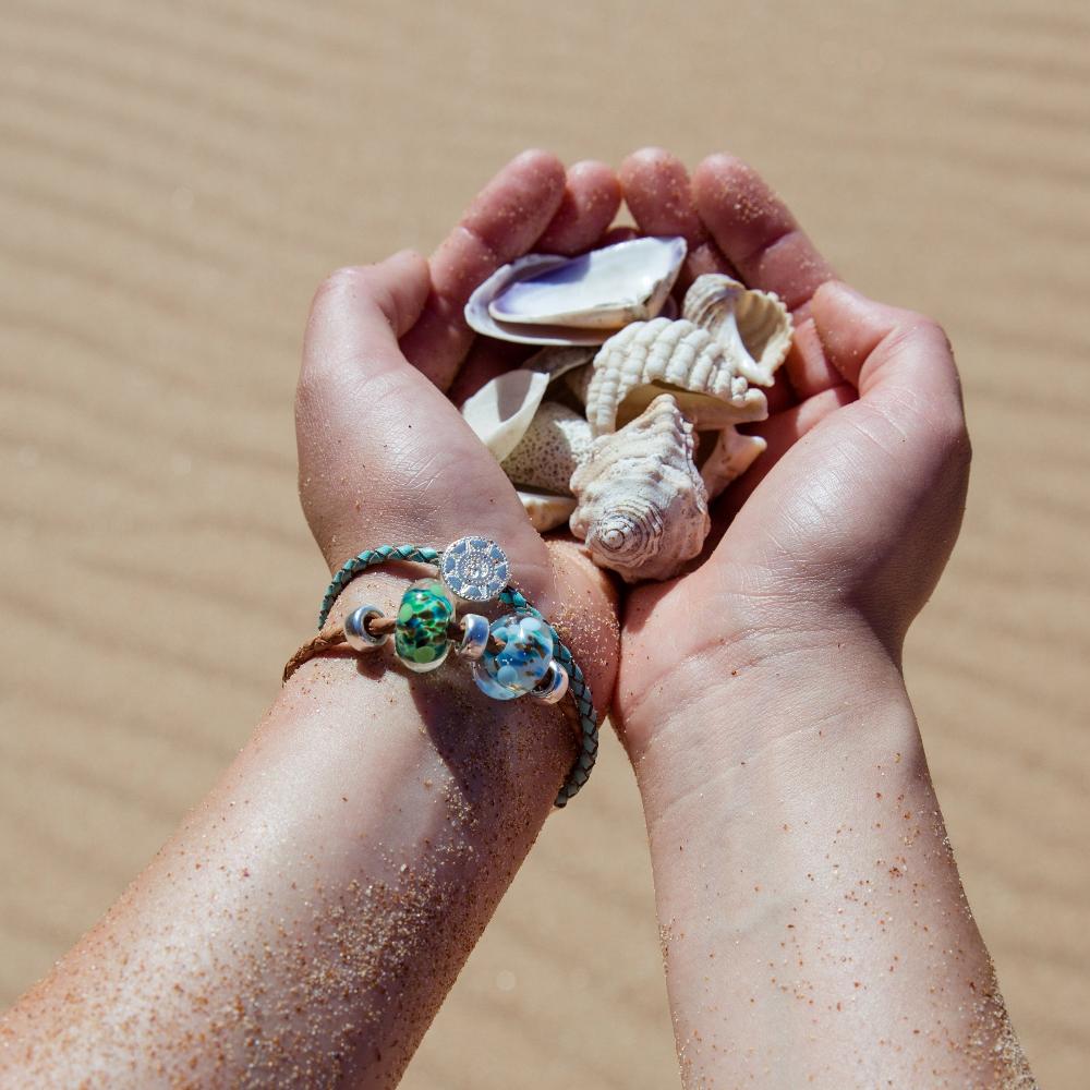 Hands holding shells, wearing leather beaded bracelets on the beach.