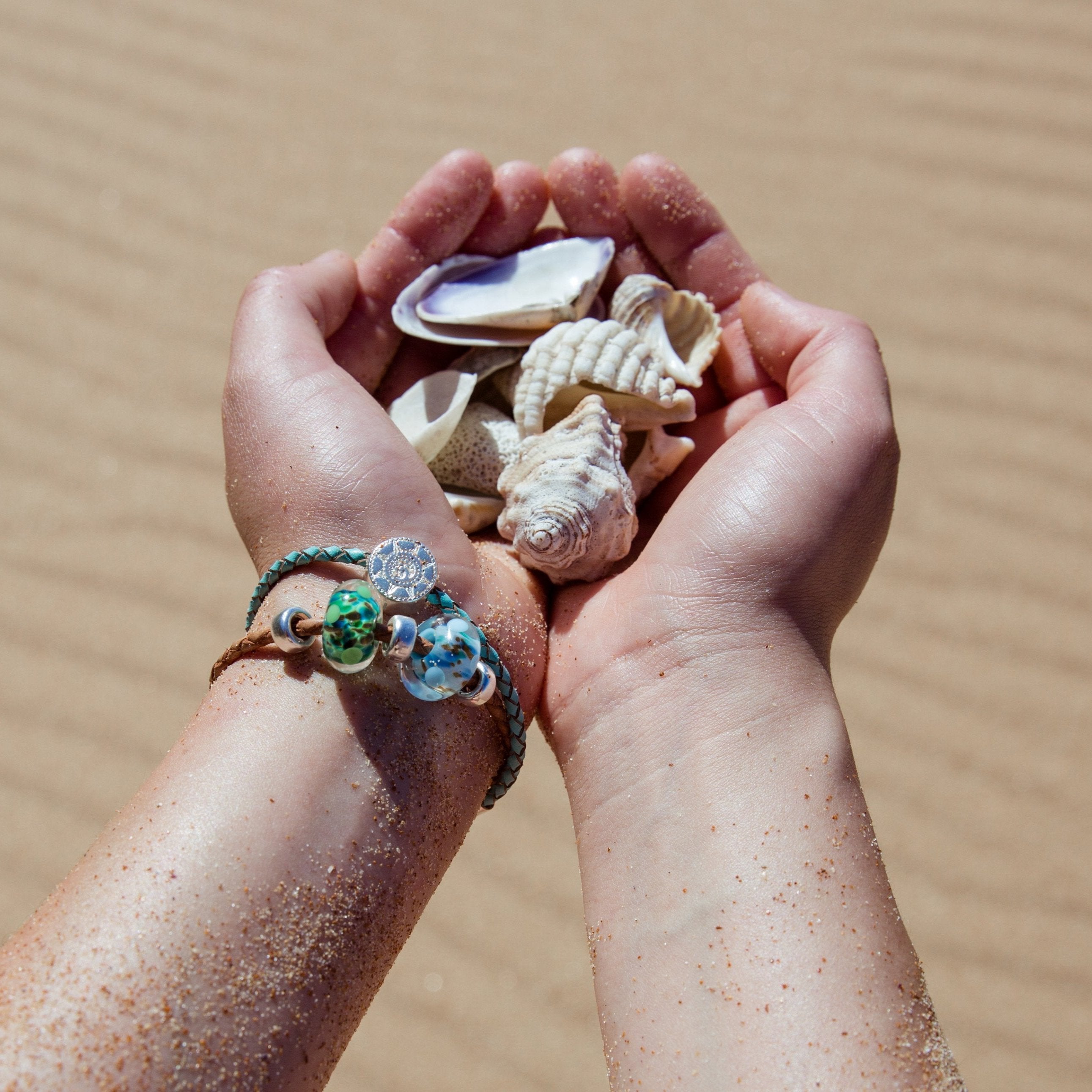 Person holding shells in their hands while wearing Nalu silver and leather beaded bracelets.