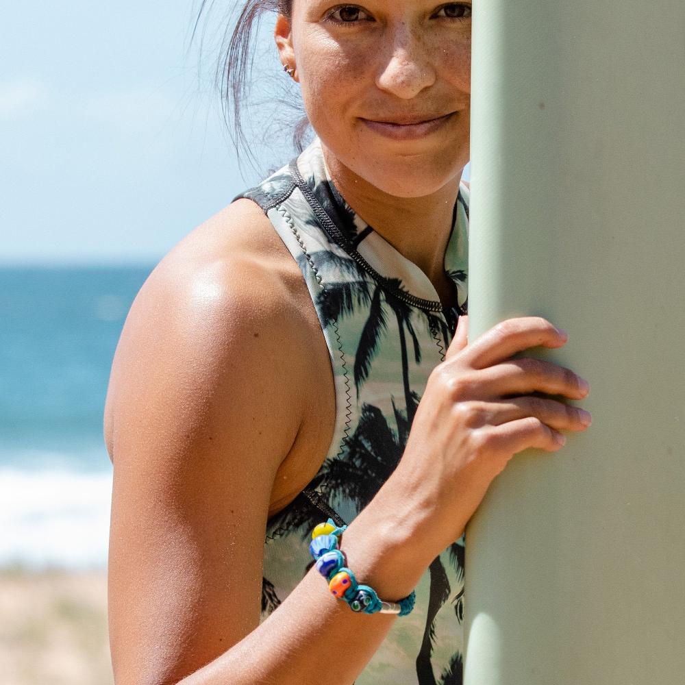 Surfer holding board wearing a teal cord bracelet.