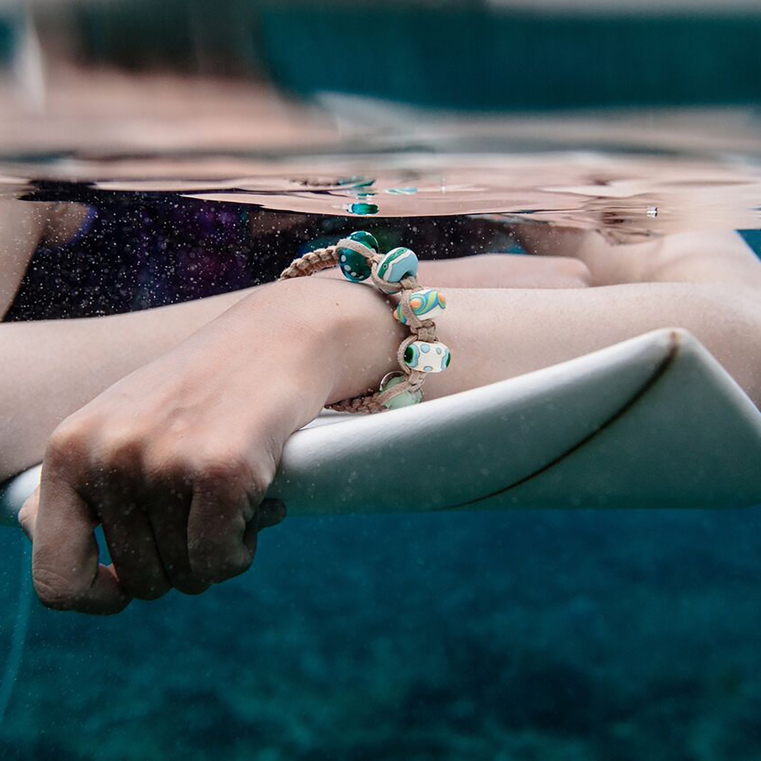 Woman surfer wearing Nalu beads bracelet in sea.