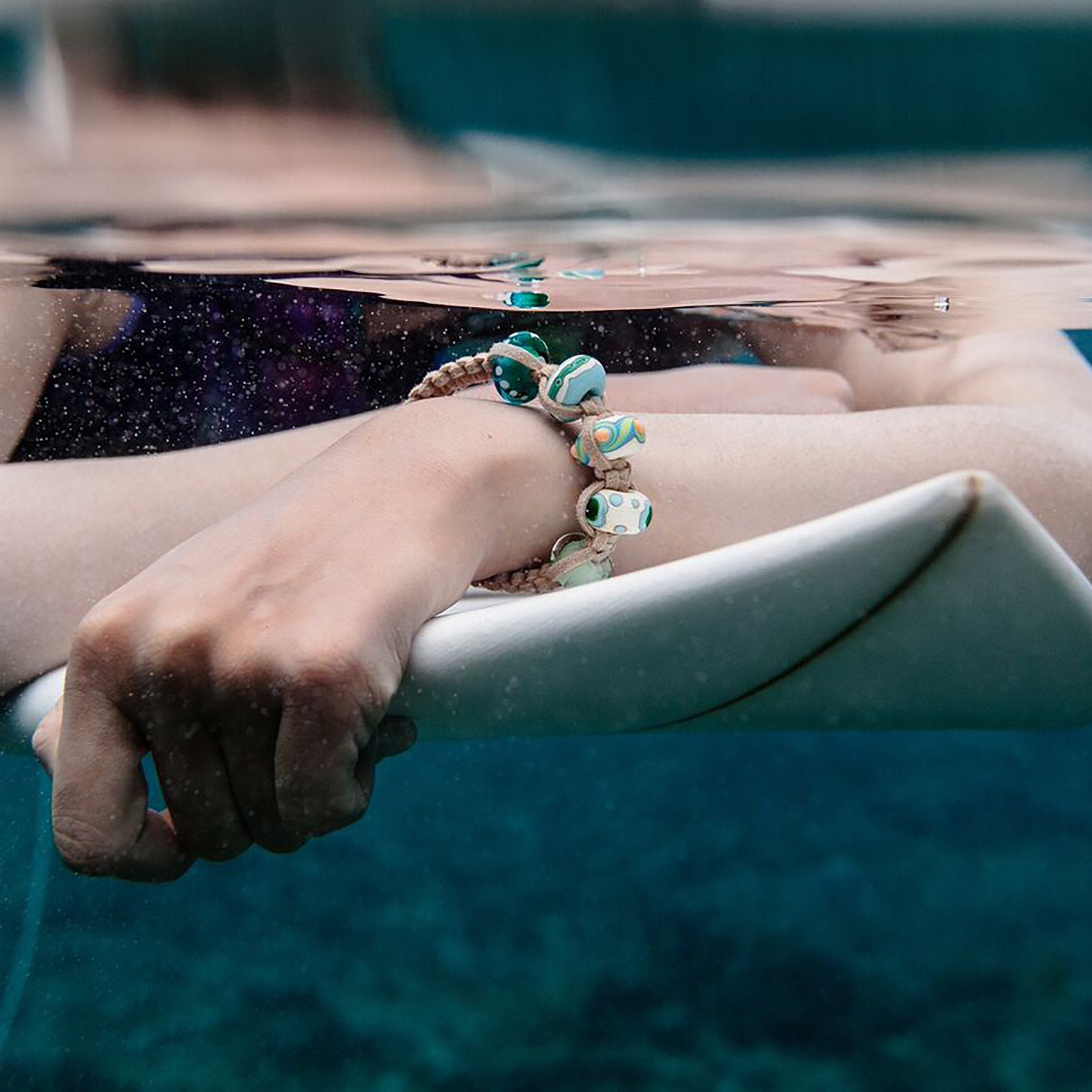 Surfer on a board in the sea wearing a bead bracelet.