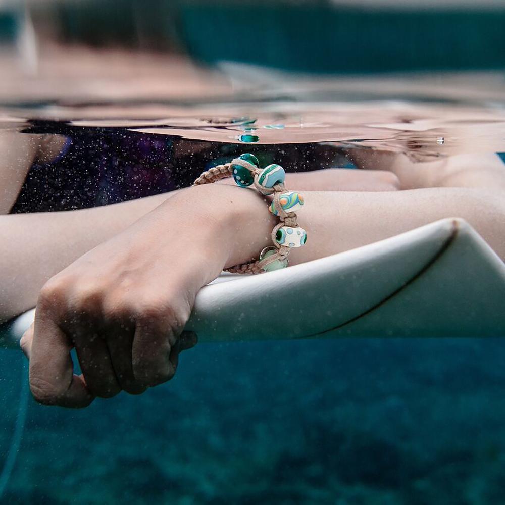 Surfer woman wearing beaded bracelet, sitting on surfboard in the sea in FIJI.