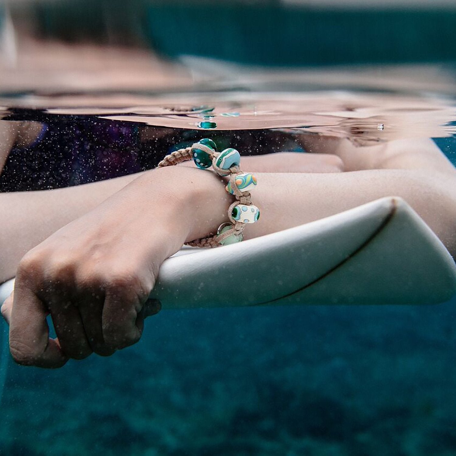 Surfer in the sea wearing a cord beaded bracelet.