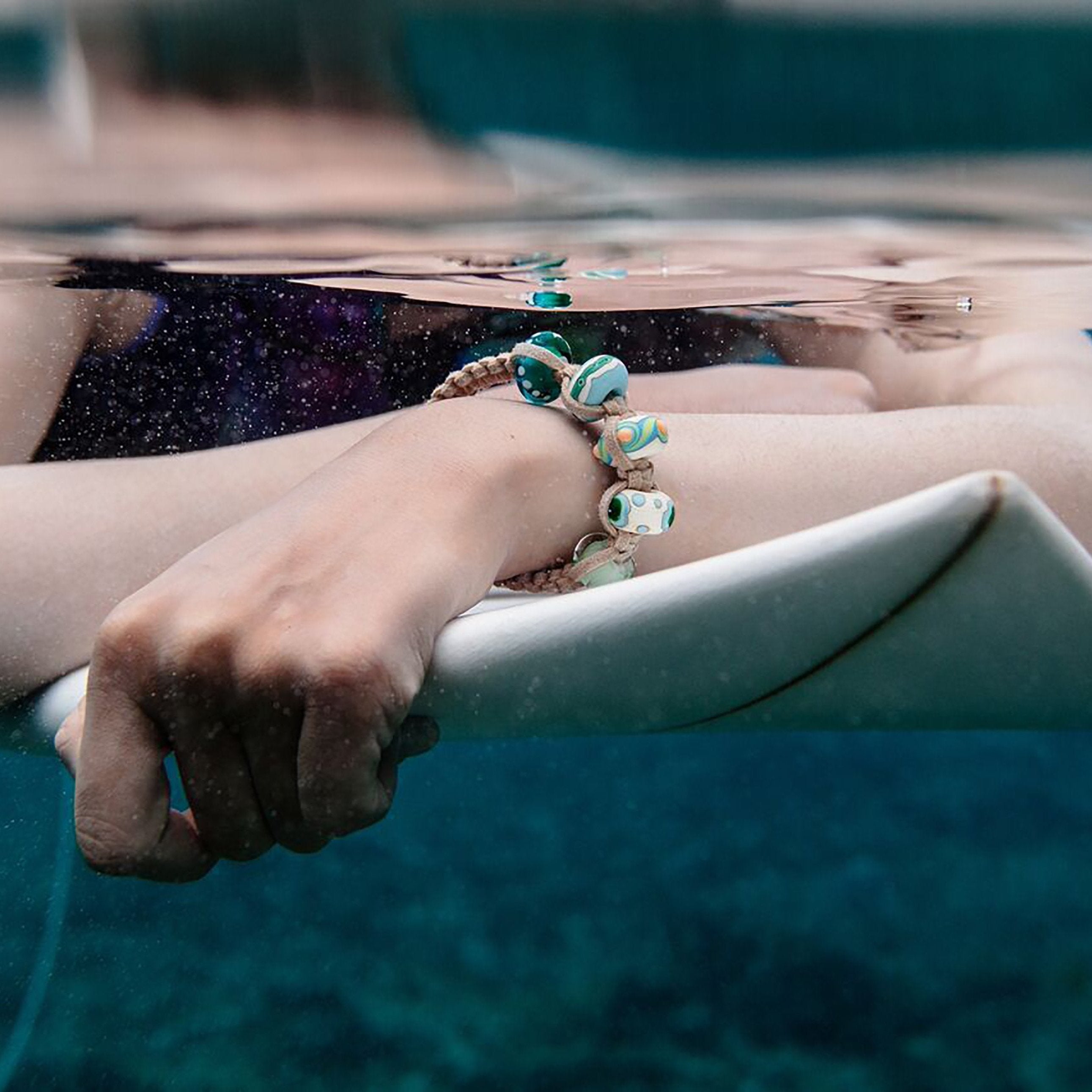 Surfer wearing beaded bracelet in sea.