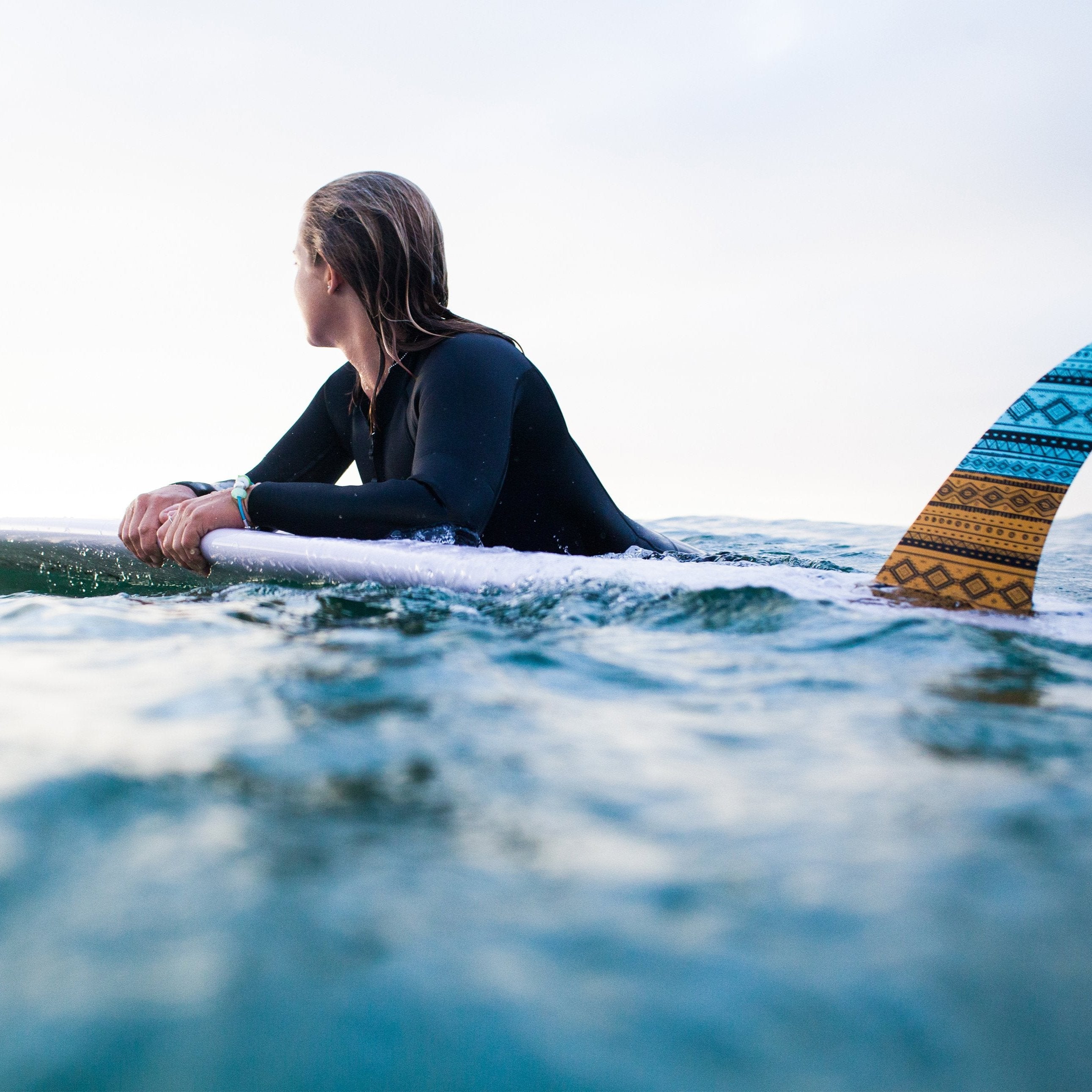 Woman wearing a wetsuit floating on surf board in the sea with a Nalu bead bracelet.