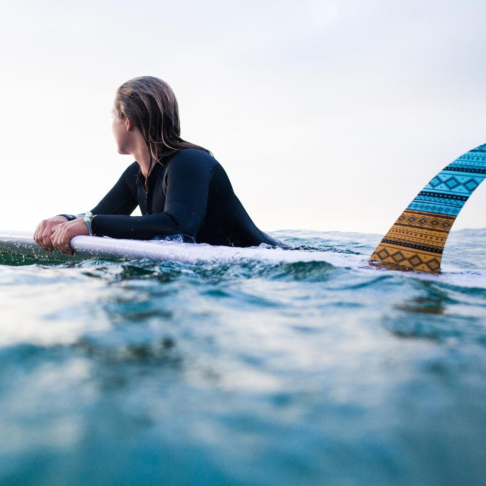 Woman wearing a wetsuit floating on surf board in the sea with a Nalu bead bracelet.