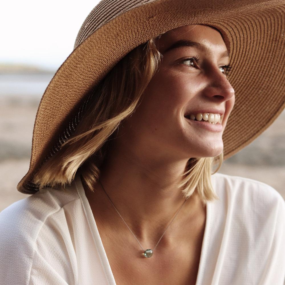 Woman in a hat wearing a glass sand pebble necklace.