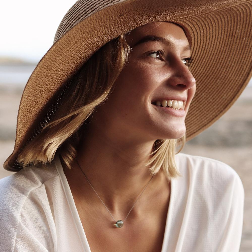 Woman in a hat wearing a glass sand pebble necklace.