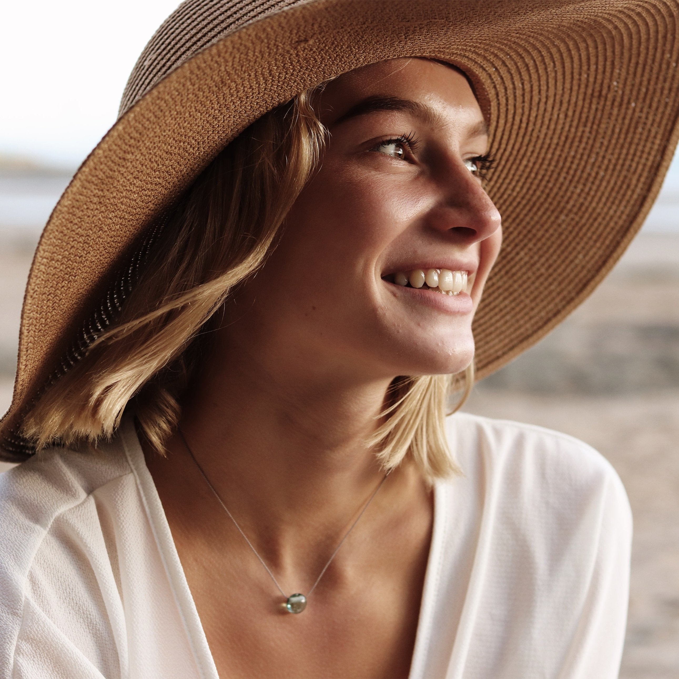 Woman in a hat wearing a glass sand pebble necklace.