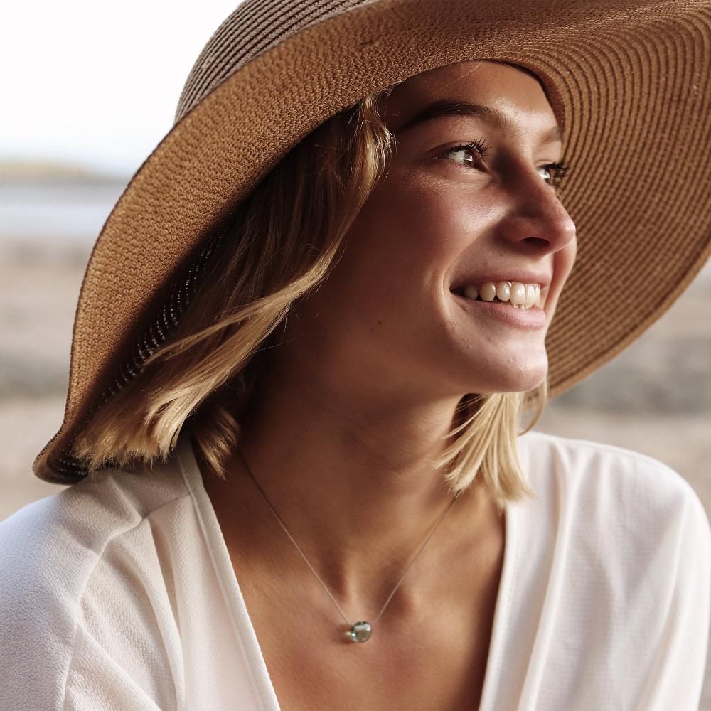 Woman in a hat wearing a glass sand pebble necklace.