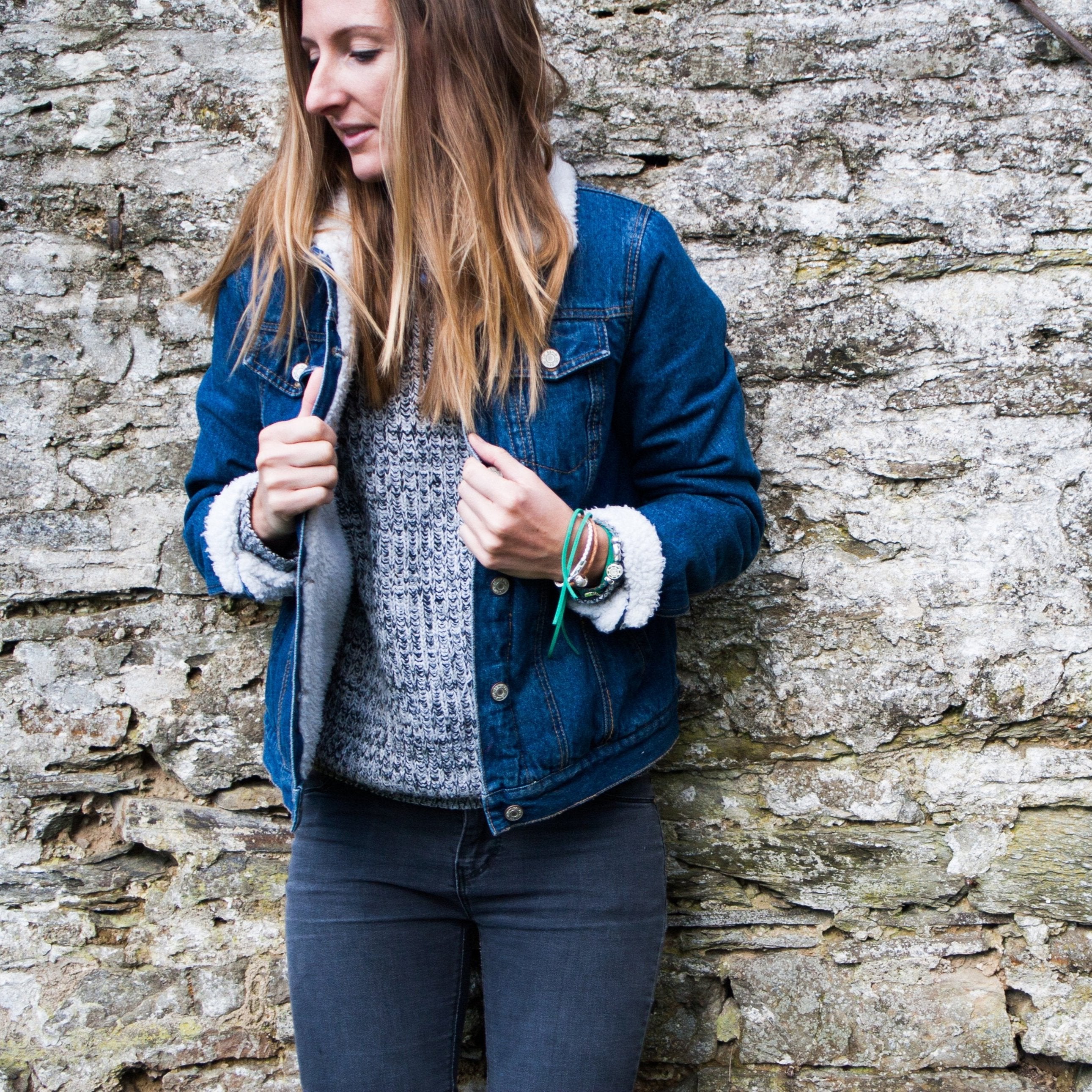 Woman in denim jacket standing in front of a stone wall.