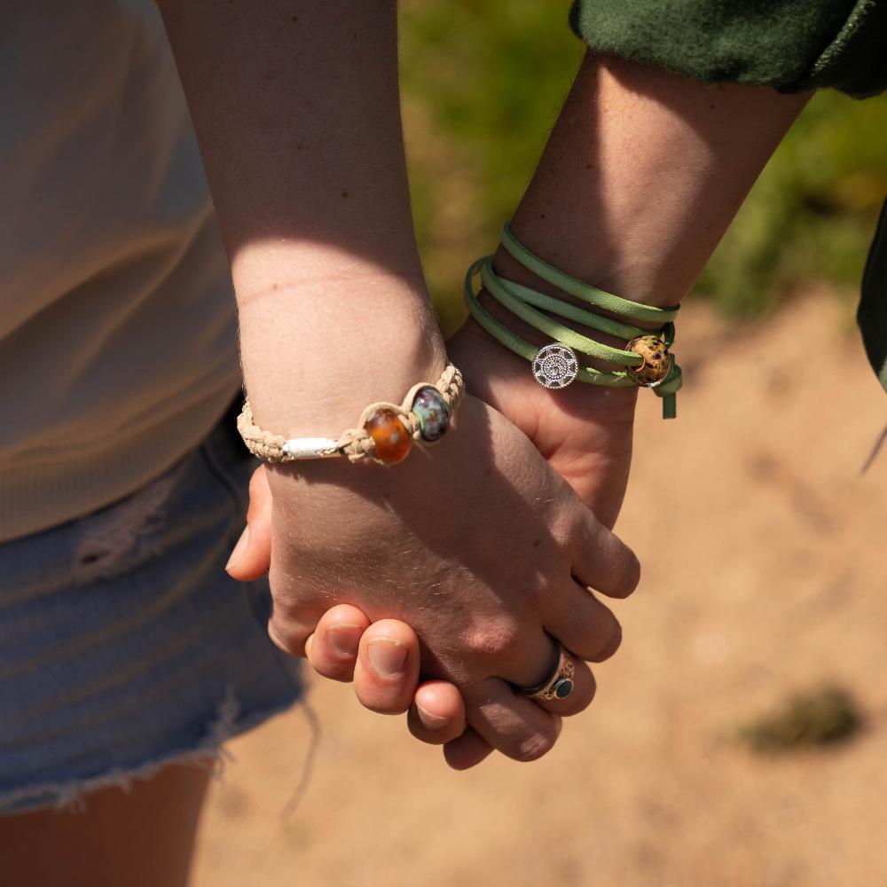 People holding hands wearing bracelets with glass and silver charms.