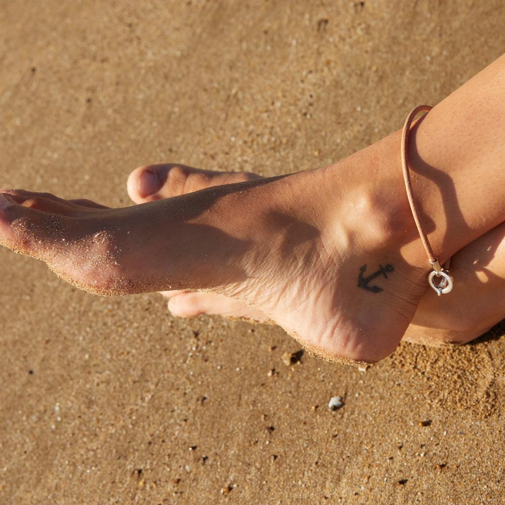 Feet crosse on the sand wearing leather anklet.