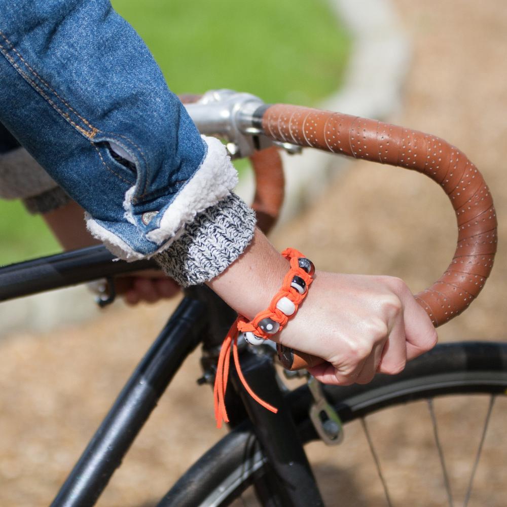 Person holding bike handle in a denim jacket wearing orange bracelet with glass beads.