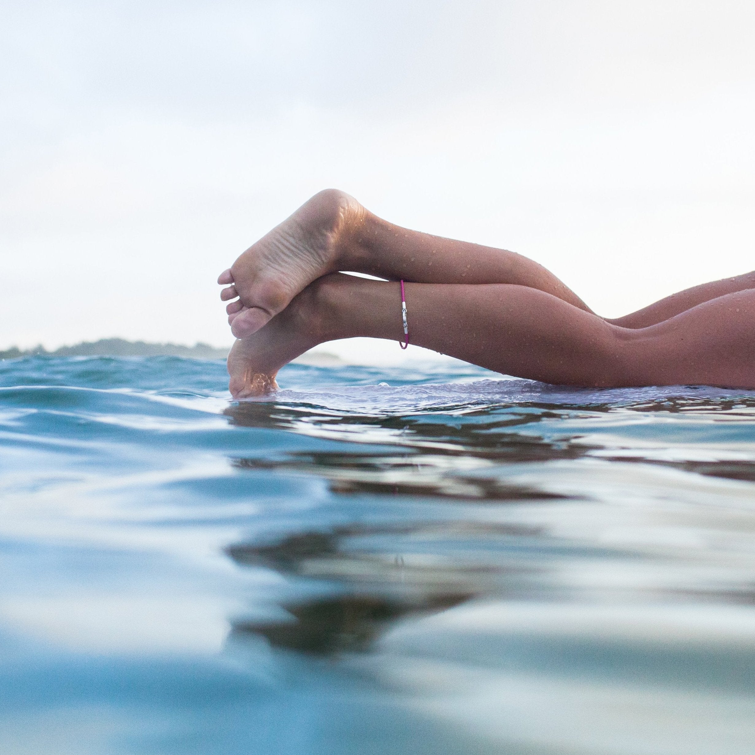 Silver North Devon Coastline bead worn on pink rubber ankle bracelet by surfer on surfboard.