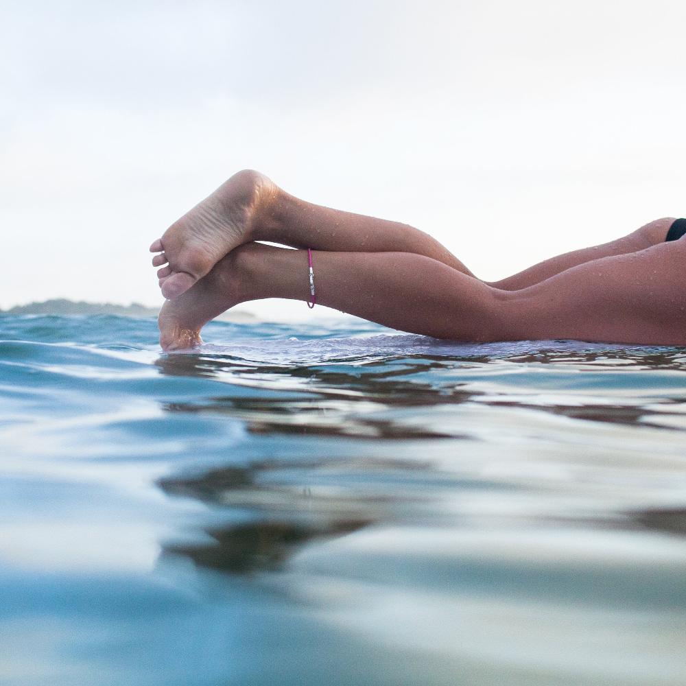 Surfer in the sea wearing a pink anklet.