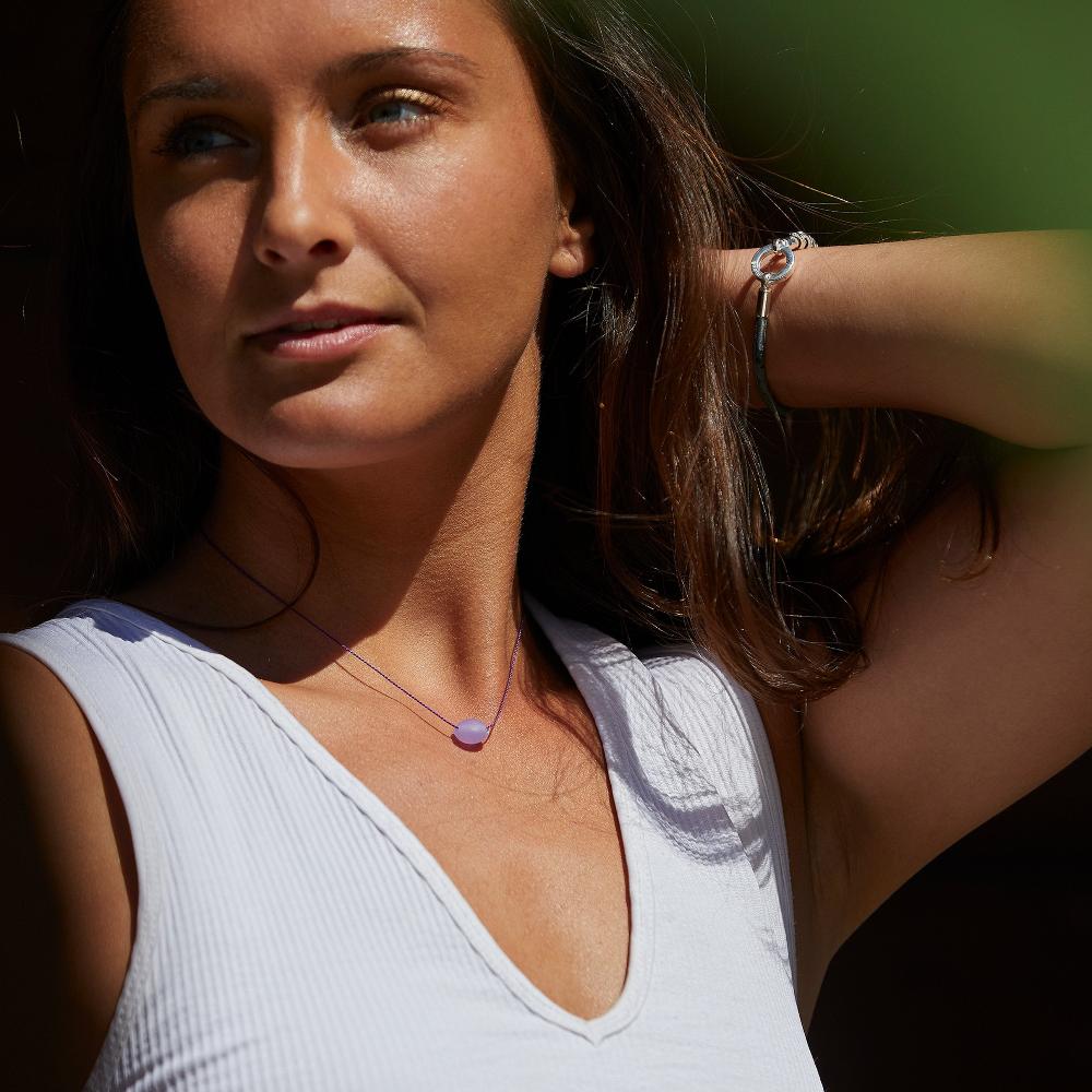 Woman wearing white vest and purple bead necklace.