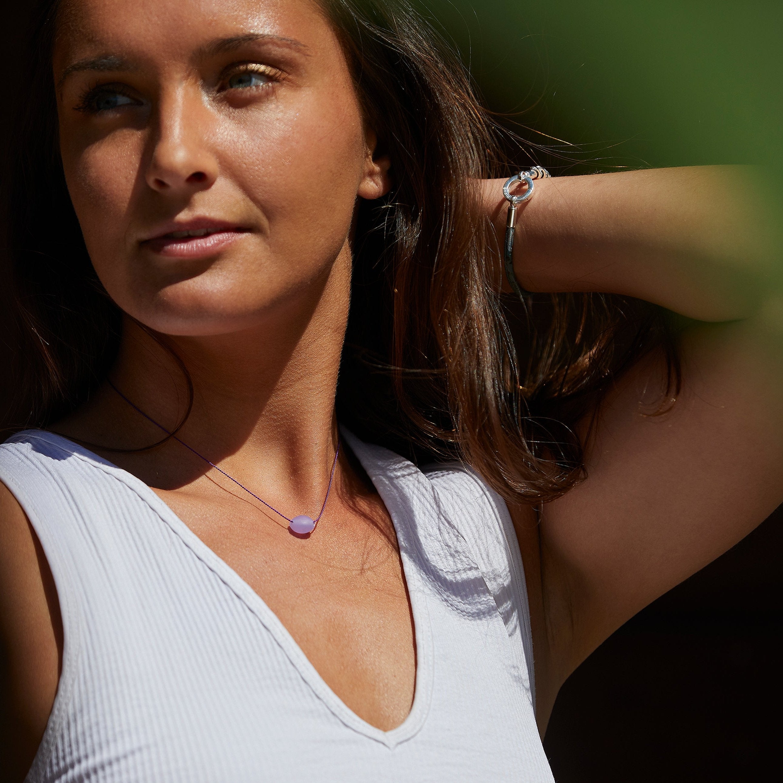 Dark haired woman wearing purple necklace and silver bracelet.