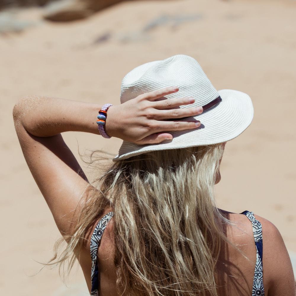 Purple bracelet worn by woman on the beach in a white beach hat.