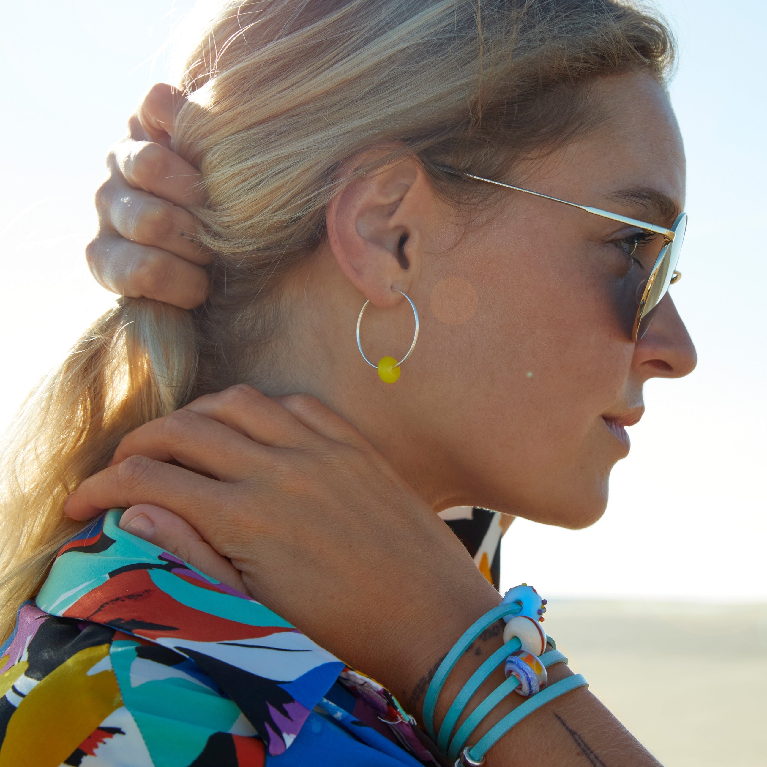 Girl wearing leather bracelet with colourful gland beads on silver hoop earrings.