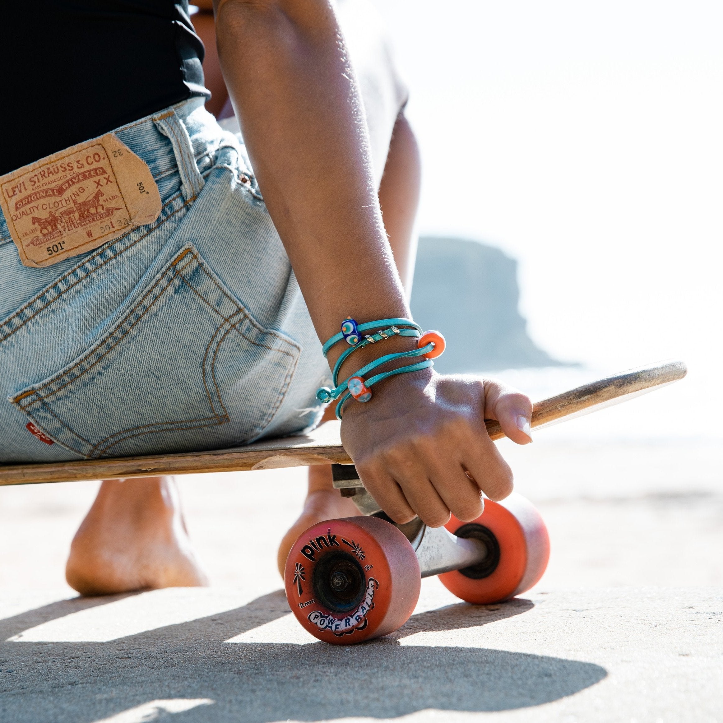 Sitting on skate board wearing turquoise leather bracelet with colourful glass beads.