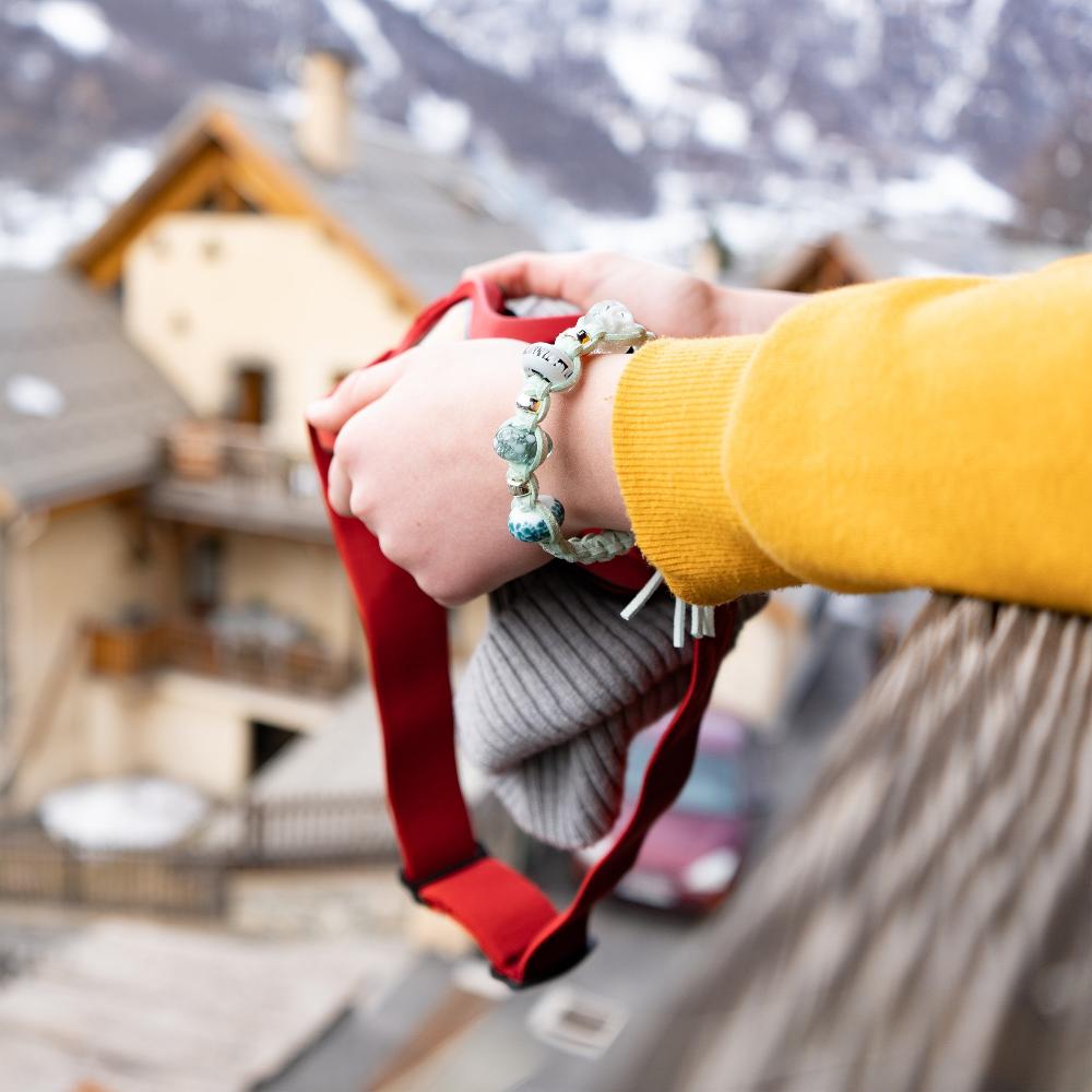 Person holding ski goggle on the balcony of French snow resort apartment, wearing a Nalu snow bead bracelet.