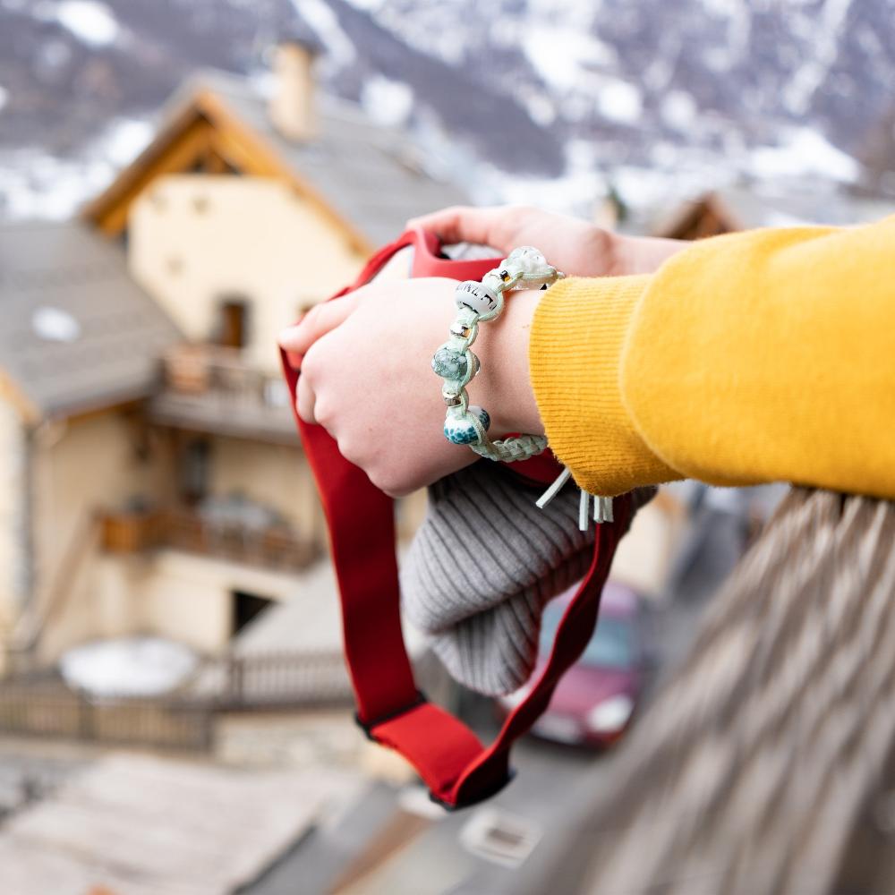 Person holding ski goggle on the balcony of French snow resort apartment, wearing a Nalu snow bead bracele