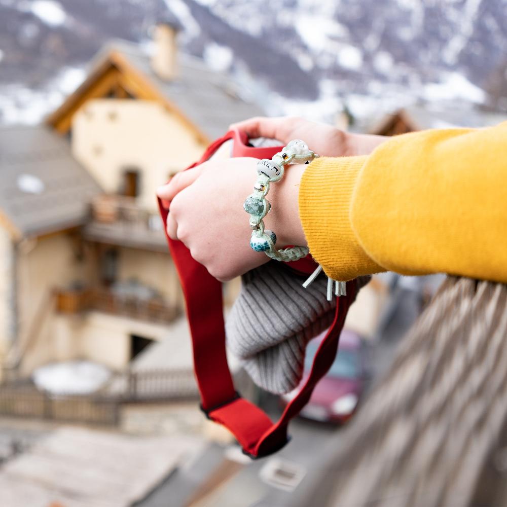 Person holding ski goggle on the balcony of French snow resort apartment, wearing a Nalu snow bead bracelet.