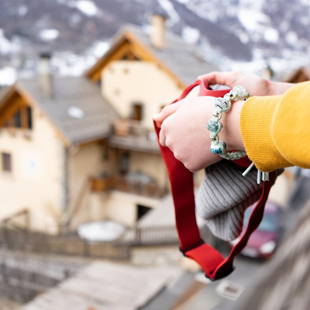 Person holding ski goggles wearing cord bead bracelet in the mountains.