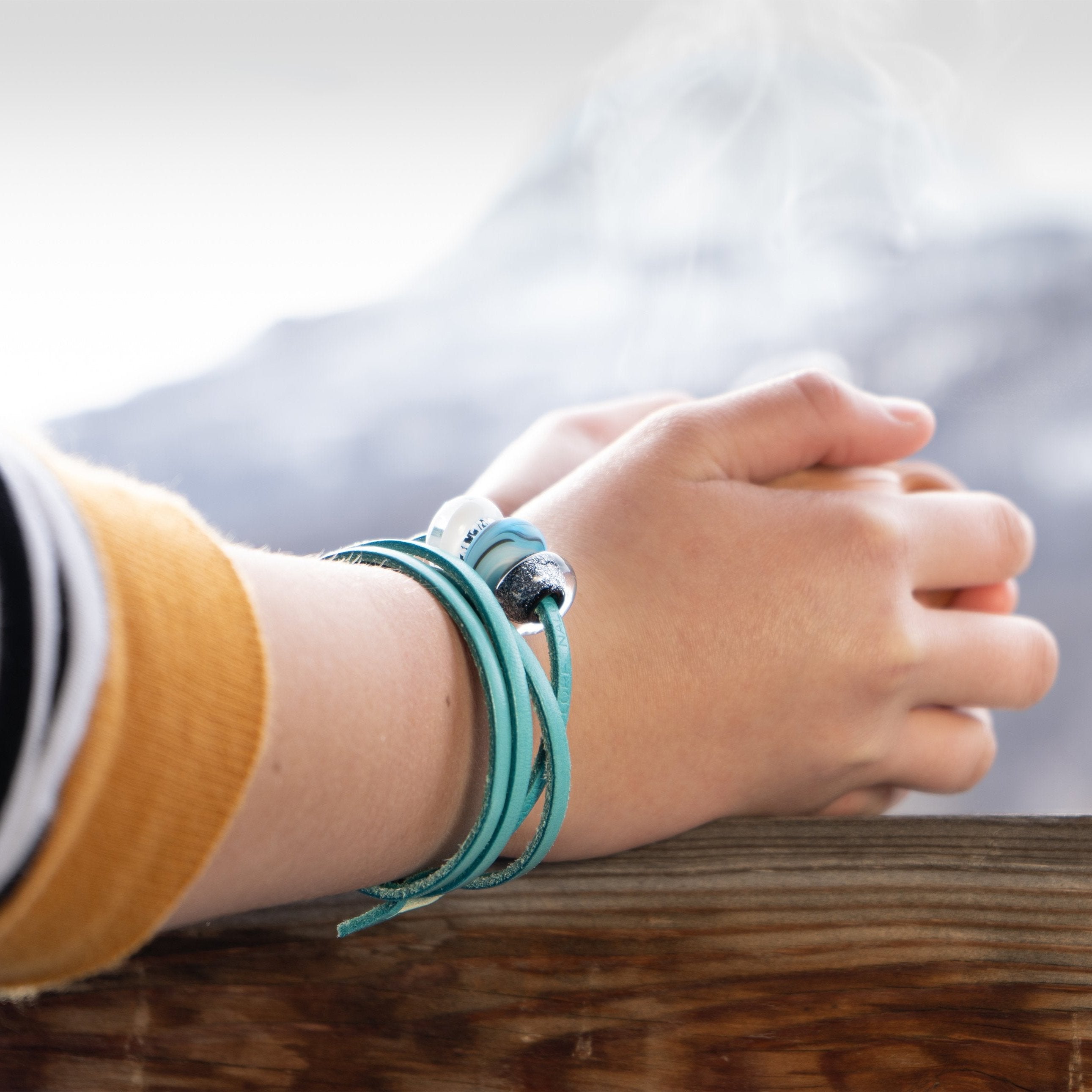 Person wearing turquoise leather wrap bracelet with Snow beads representing French alp resorts.