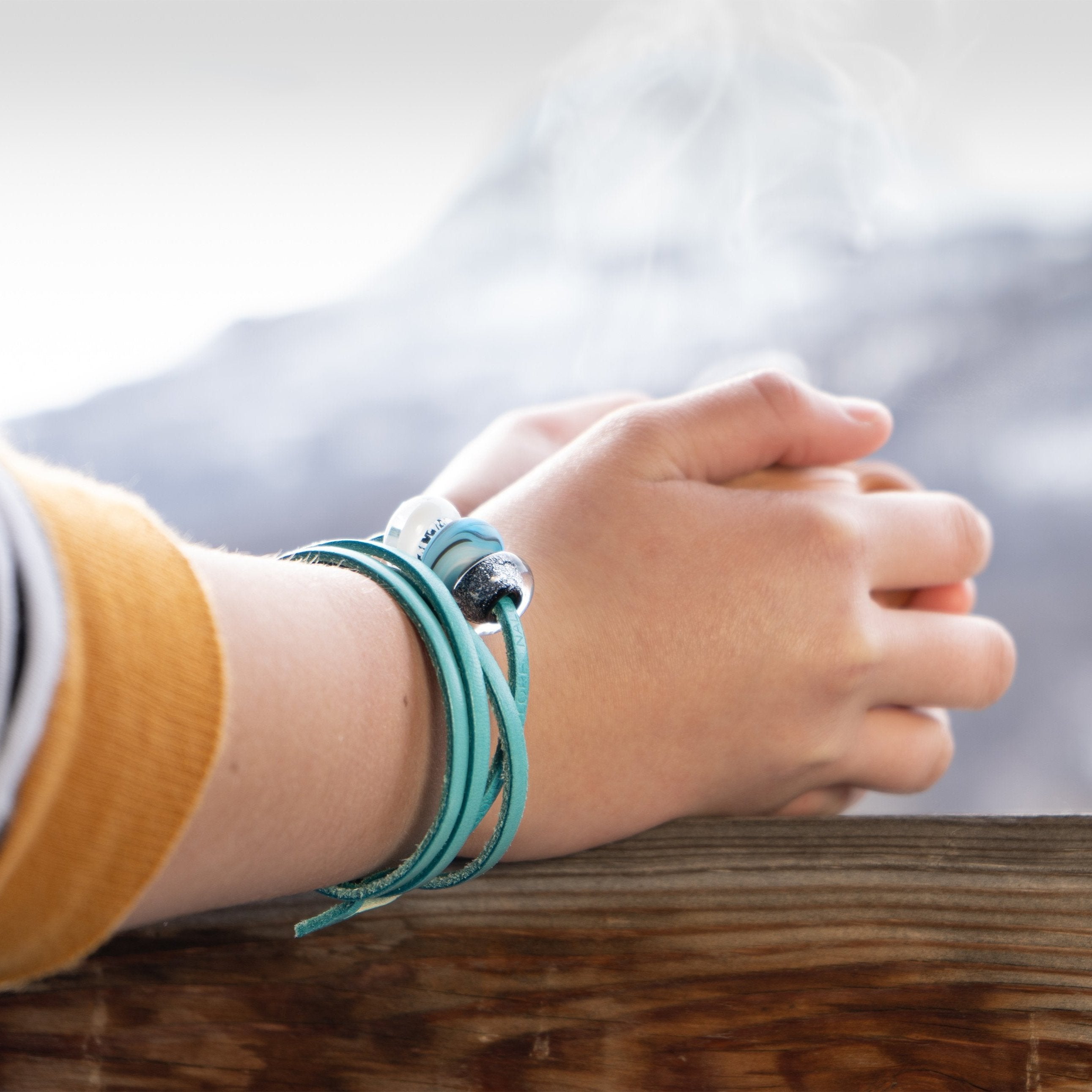 Black sparkling glass bead worn on turquoise leather wrap bracelet, holding a coffee whilst looking at the snow mountains.