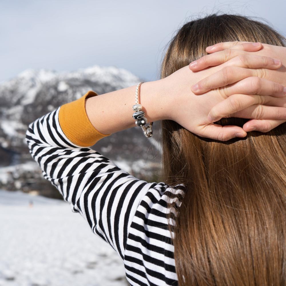 Girl in front of snow mountain wearing beaded bracelet and white and black stripe top