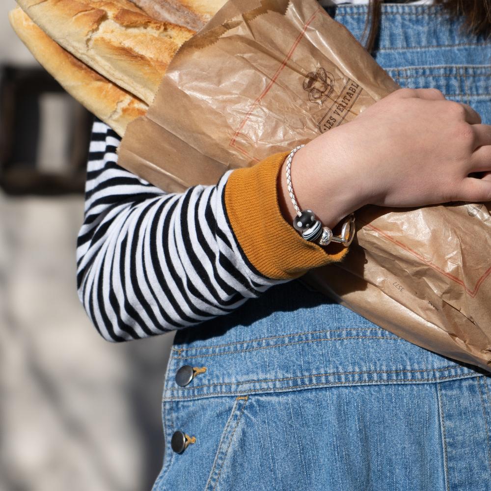 Person wearing black and white carrying bread in the French alps, wearing glass bead leather bracelet.