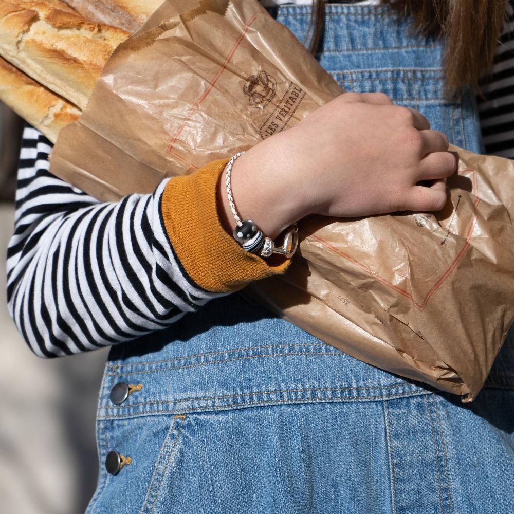 A girl carrying loaves of bread in denim dungarees wearing a white plaited bracelet with black and white glass beads.